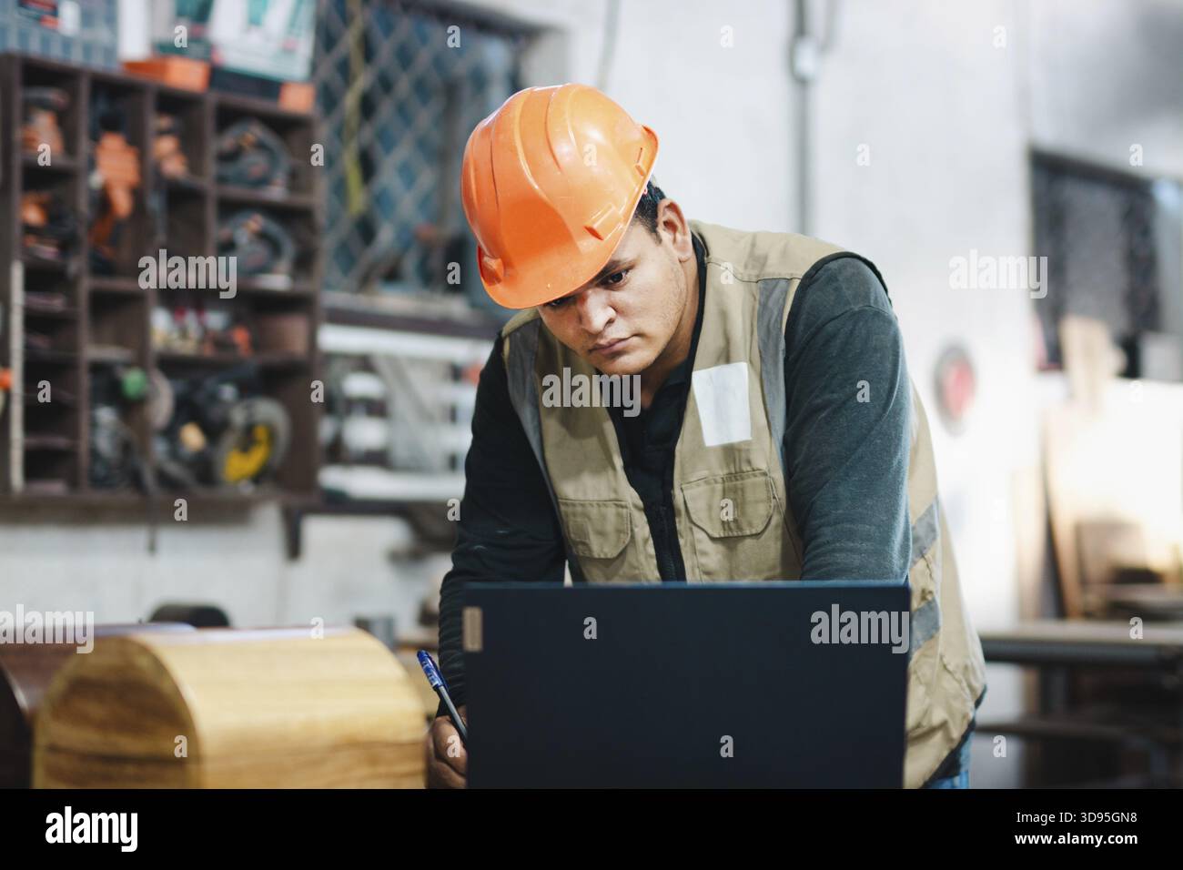 Carpenter using a laptop at a workbench in the workshop. Successful worker using a computer in the carpentry workshop Stock Photo