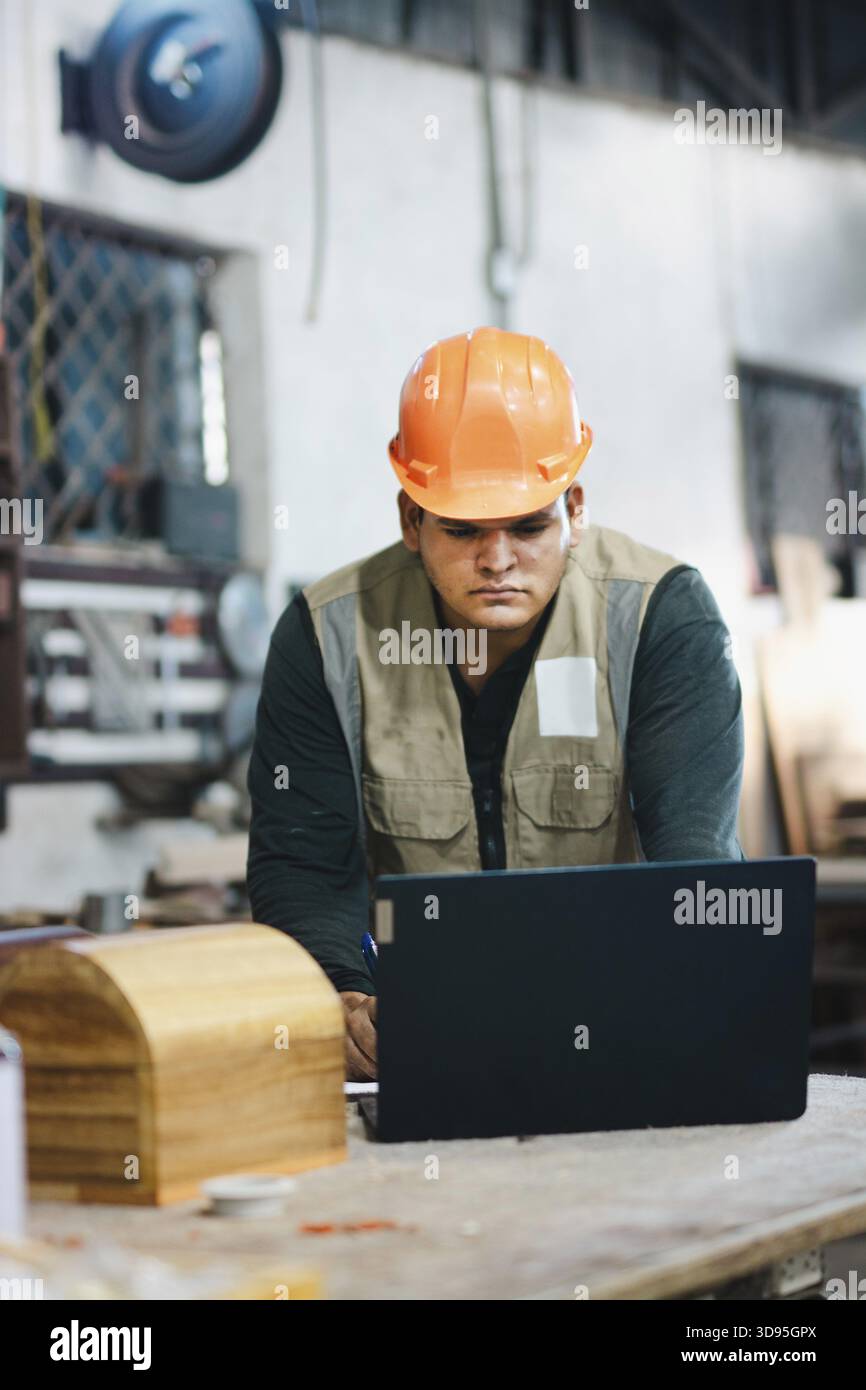 Successful worker using a computer in the carpentry workshop. Carpenter using a laptop at a workbench in the workshop Stock Photo