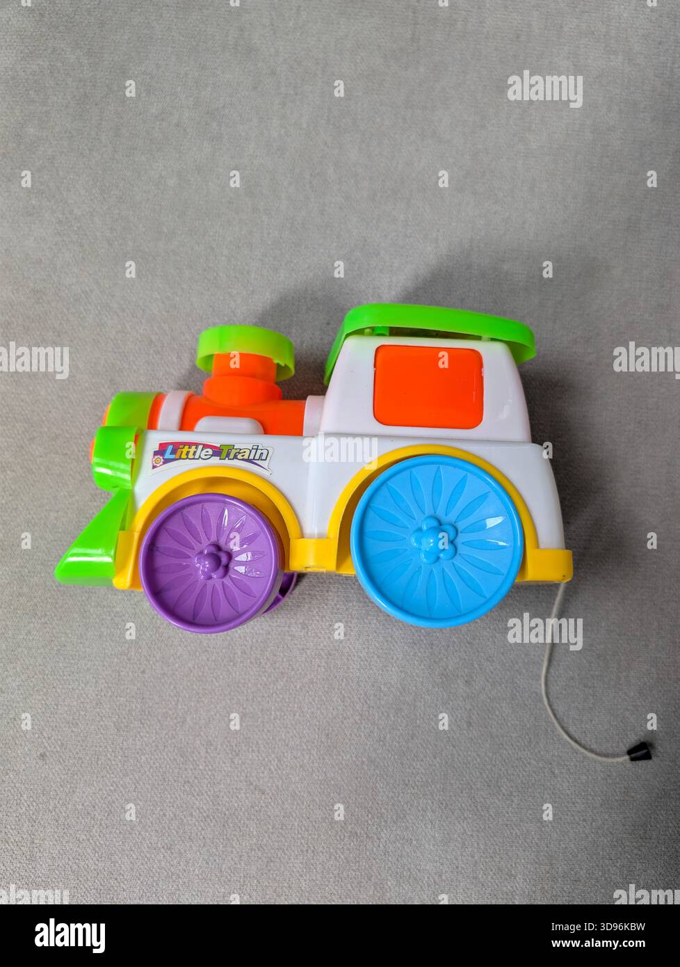Colorful plastic toy steam train engine in profile on a grey background. A bright nursery locomotive model for childhood play and education concepts. - Smartphone Captured Stock Image