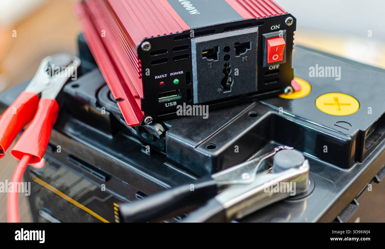 A close-up shot of a  red and black power inverter connected to a car battery using heavy-duty jumper cables with alligator clips. The inverter featur Stock Photo
