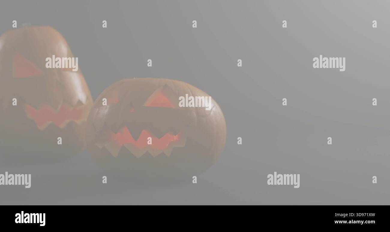 Glowing carved pumpkins emitting warm orange light in dim foggy studio on matte surface, copy space Stock Photo