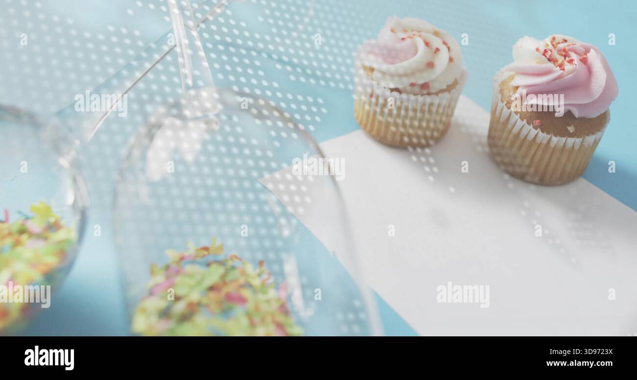 Showing two sprinkled cupcakes on pastel-blue table, inverted glasses, dotted light, copy space Stock Photo