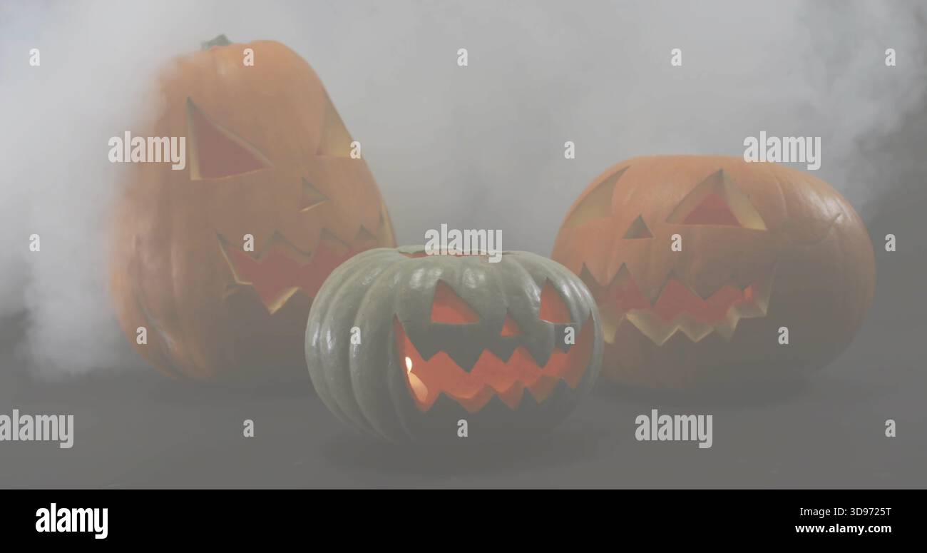 Glowing three carved pumpkins emitting warm inner light on dark tabletop with drifting smoke Stock Photo