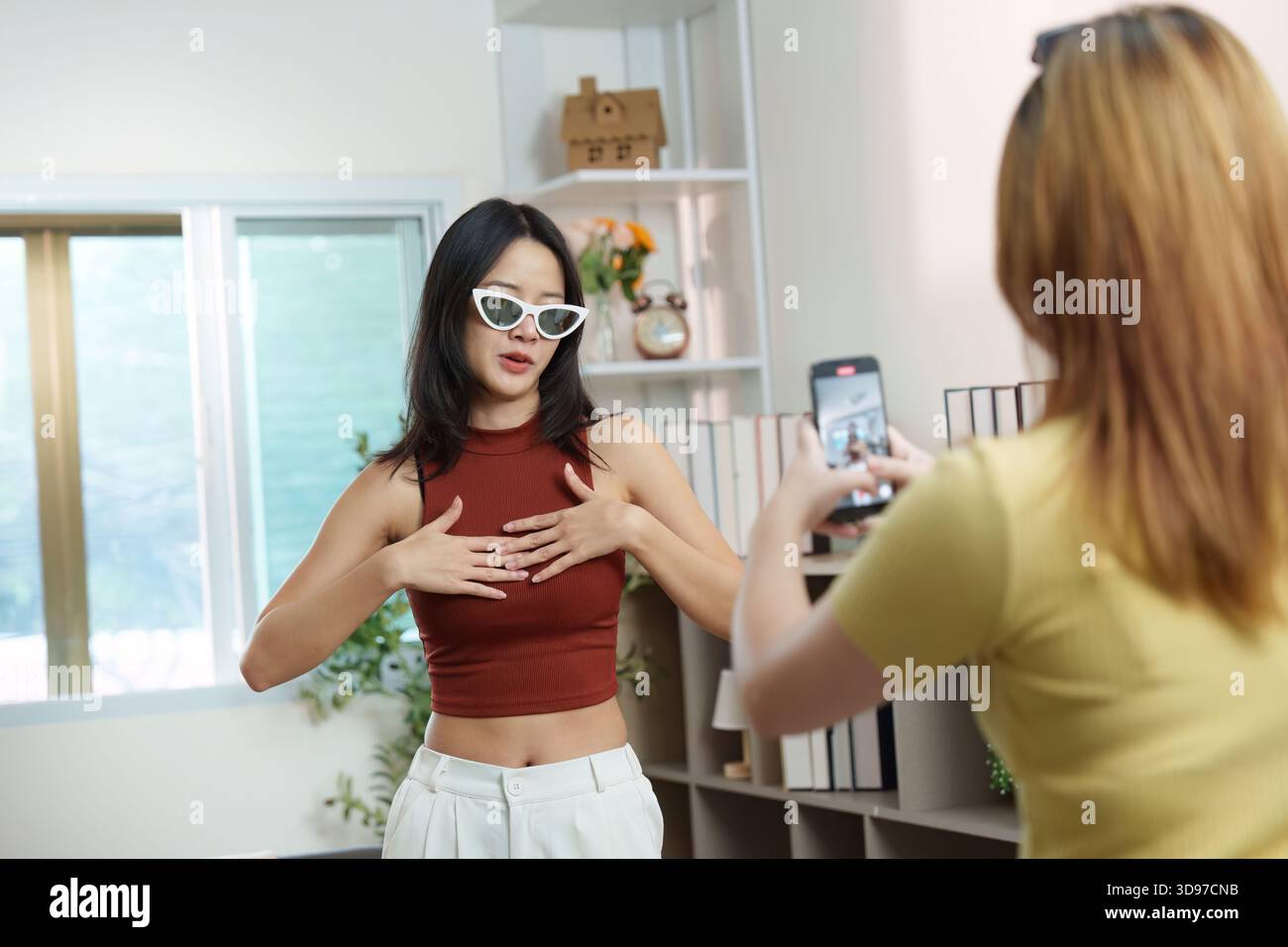 Social Media. A young woman showcasing her outfit while her friend records her indoors. Stock Photo