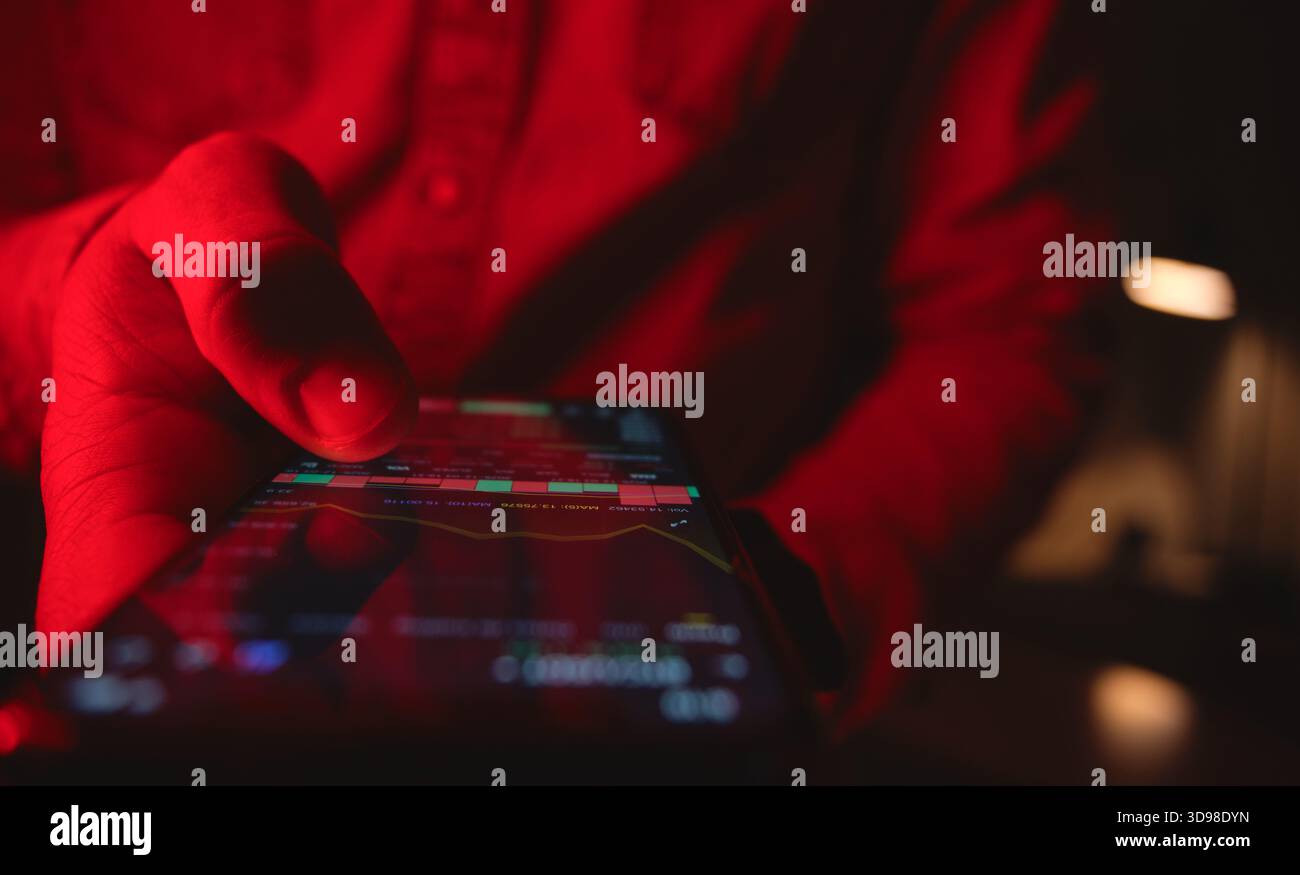 Hand holding phone while tracking stock market data and investment performance in red light Stock Photo