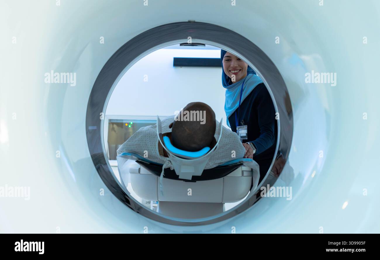 African American woman patient lying with blue head pad entering CT gantry while woman tech guiding Stock Photo