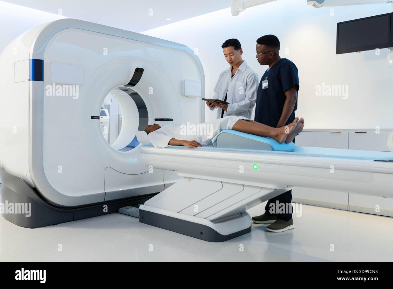 CT scanner gantry rotating while motorized exam table sliding into bright radiology suite Stock Photo