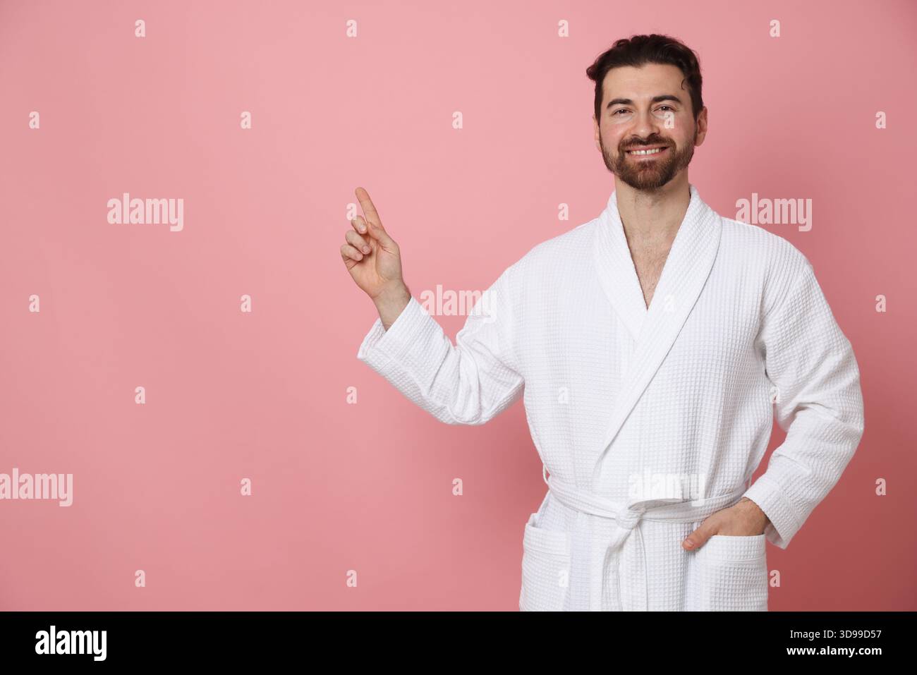 Man in bathrobe pointing at something on pink background. Space for text Stock Photo