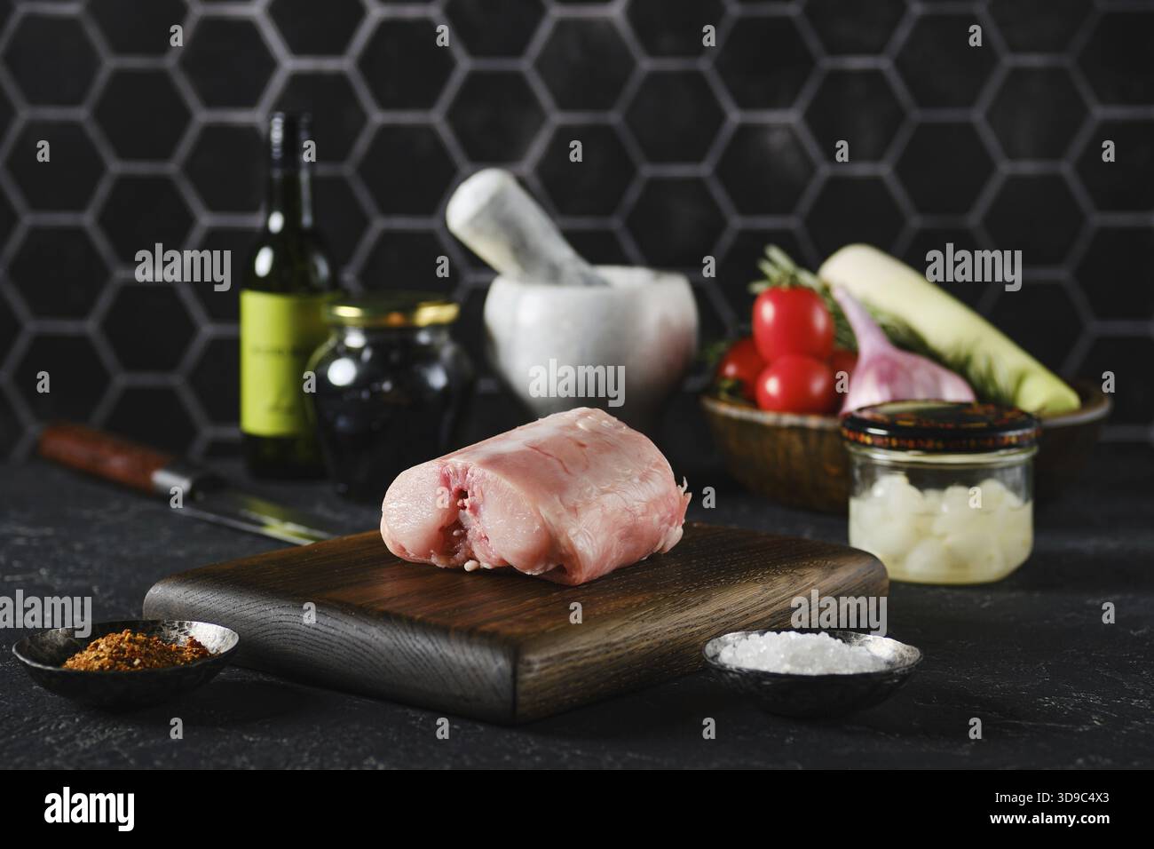 A fresh rabbit saddle on a wooden cutting board surrounded by fresh vegetables and cooking tools Stock Photo