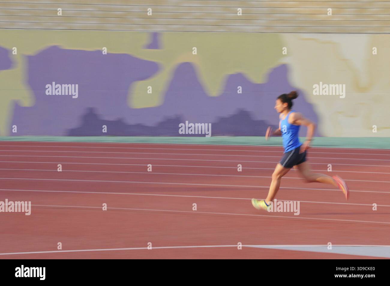 Young female athlete is running fast on a track and field stadium track ...
