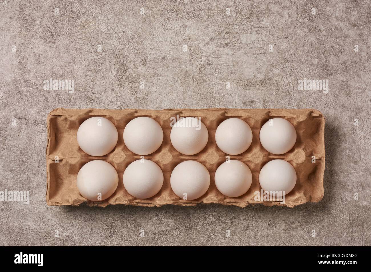 top view of ten fresh white eggs in cardboard carton textured gray stone background, copy space for text, healthy protein and breakfast concept Stock Photo