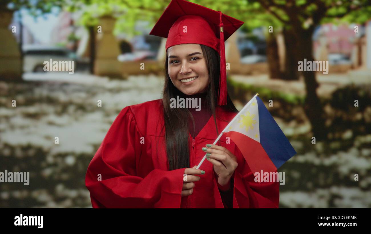 Woman in red graduation gown holding philippine flag in a park setting, symbolizing accomplishment, pride, and national identity. Stock Photo