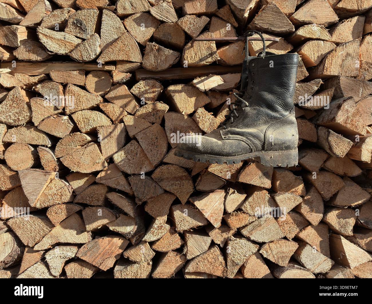 Vintage Worn Black Work Boot Against Rustic Woodpile Background - for themes of forestry, craftsmanship, rural life, outdoor work, sustainability. - Smartphone Captured Stock Image