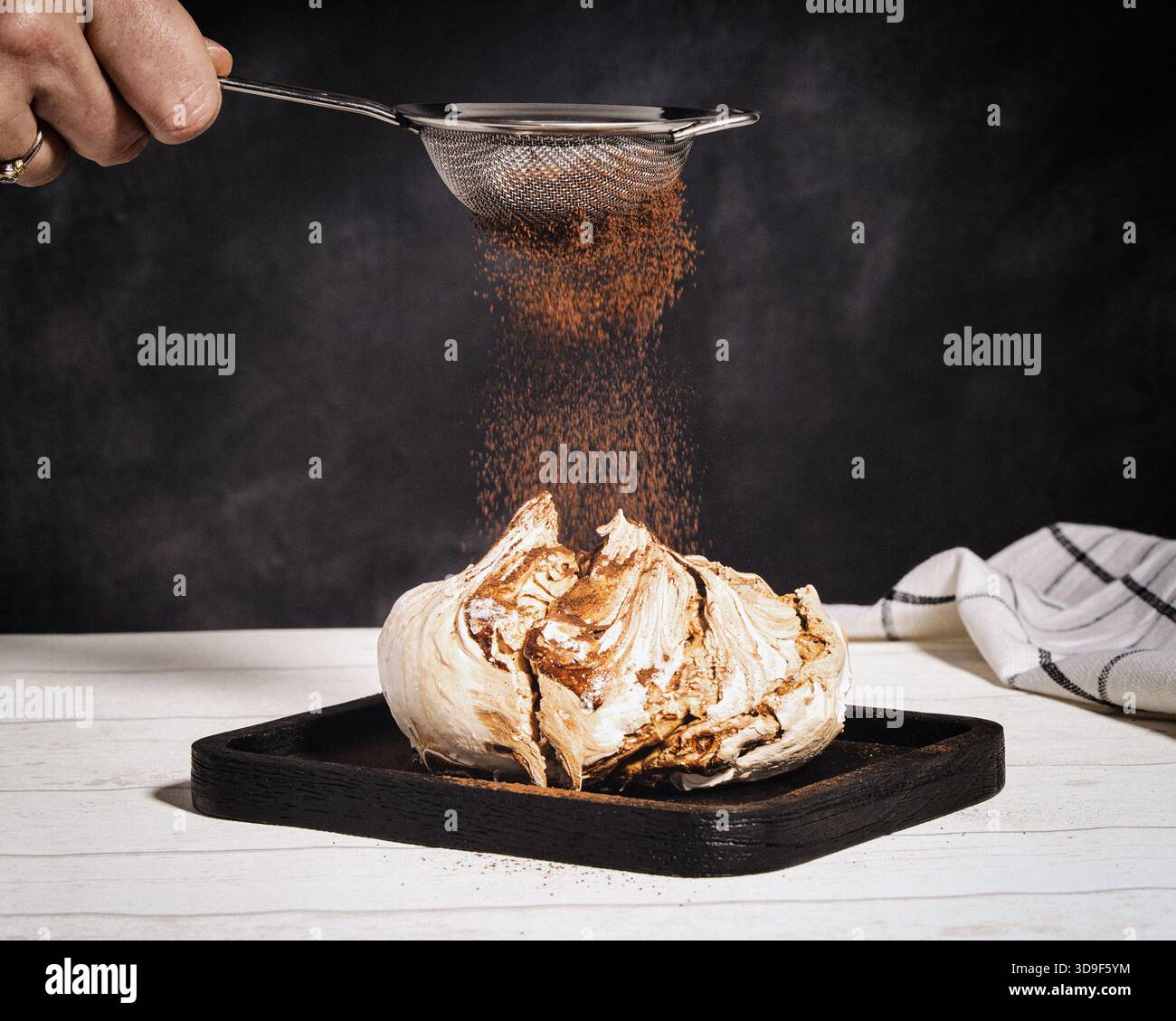 coco powder being sieved over a chocolate meringue Stock Photo - Alamy