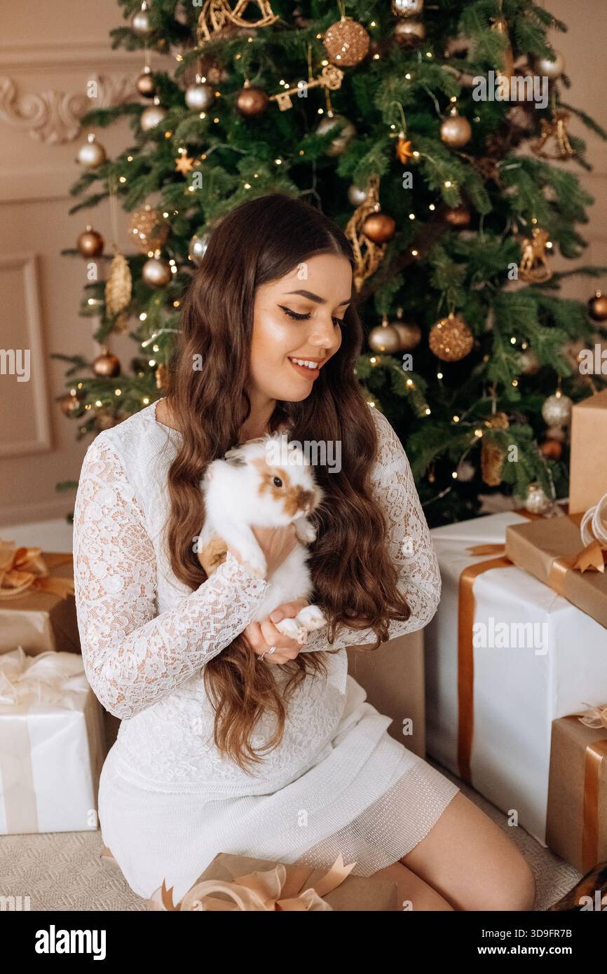 A joyful woman is sitting on the floor, cradling an adorable rabbit while smiling. Stock Photo