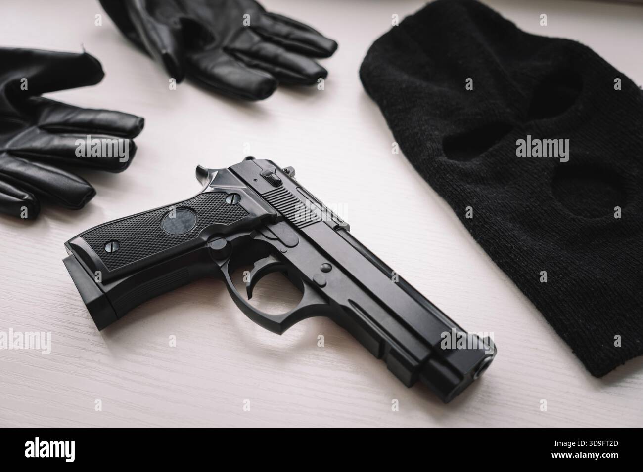 Gloves, a pistol and a black mask on a white table. Evidence during the search of a robber or murderer. evidence of a crime. Stock Photo