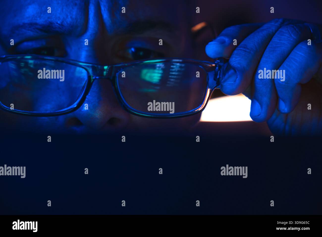 Person removing glasses while looking at data illuminated by blue screen light Stock Photo