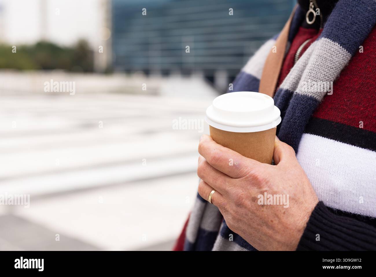Man standing on urban plaza holding takeaway coffee cup while wearing striped sweater, copy space Stock Photo