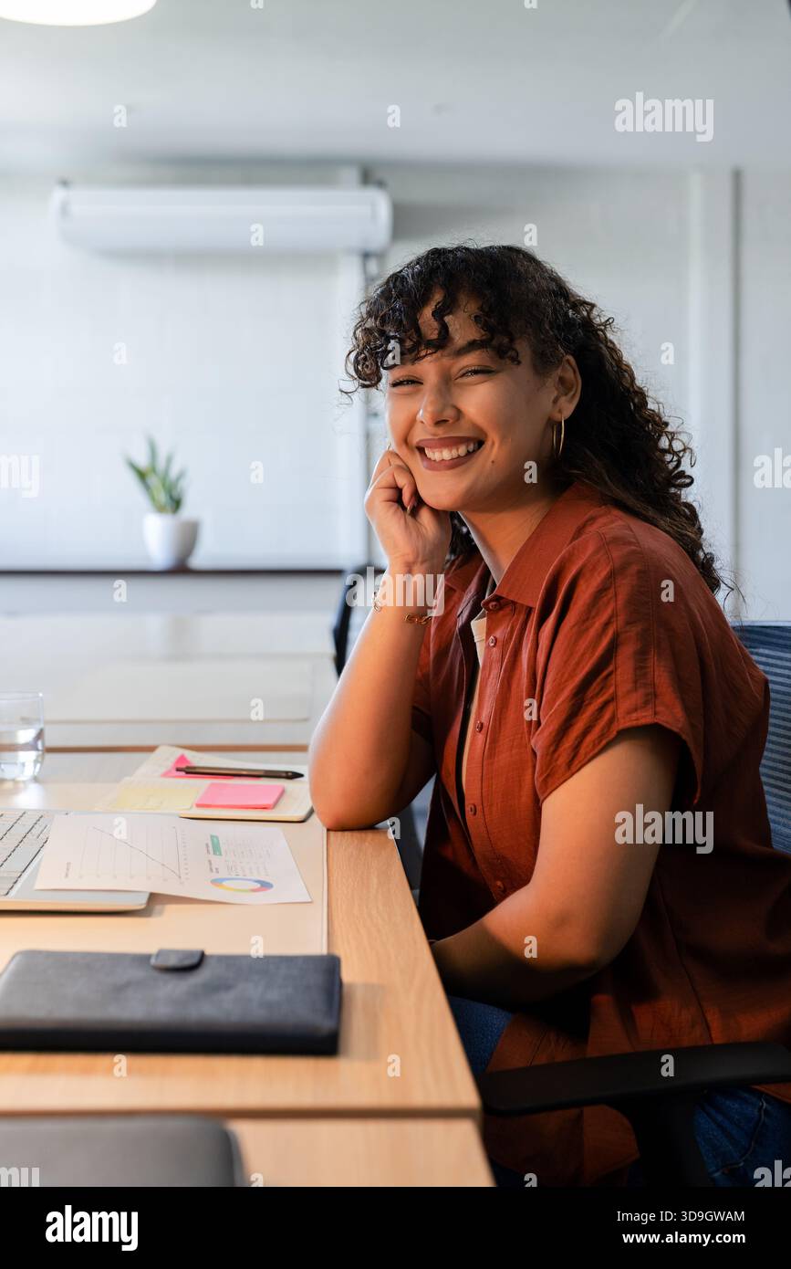 Smiling African American woman in rust shirt at desk with laptop and charts, copy space Stock Photo