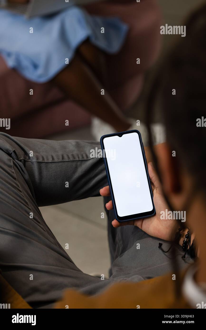 Smartphone is resting on gray pants with black case and blank screen in lounge, blurred sofa Stock Photo