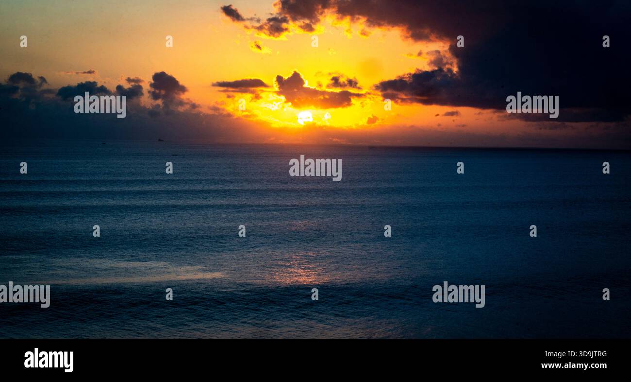 Dramatic ocean sunset with vibrant orange and dark clouds. Stock Photo