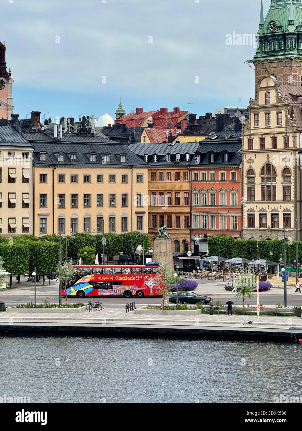 Colorful sightseeing bus passing historic buildings at the waterfront in central Stockholm, Sweden, with views of architecture of Gamla Stan. - Smartphone Captured Stock Image