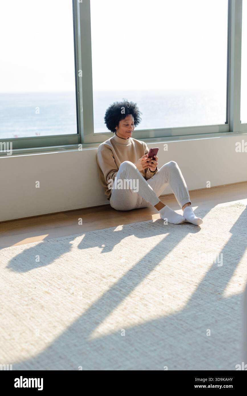 Man leaning against wall on rug overlooking ocean while using smartphone, copy space Stock Photo