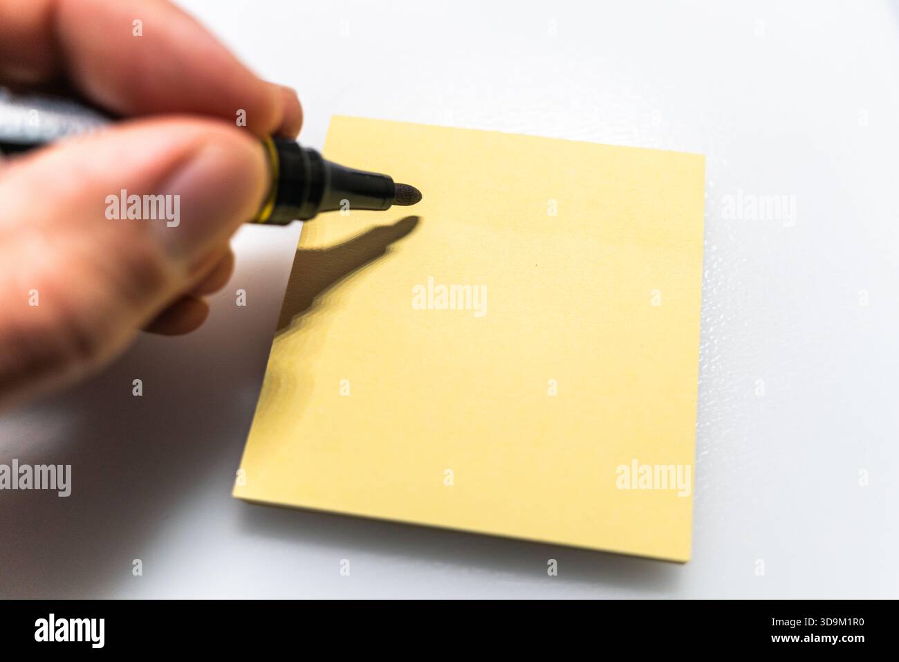 Marker in hand over empty yellow sticky note on white background Stock Photo