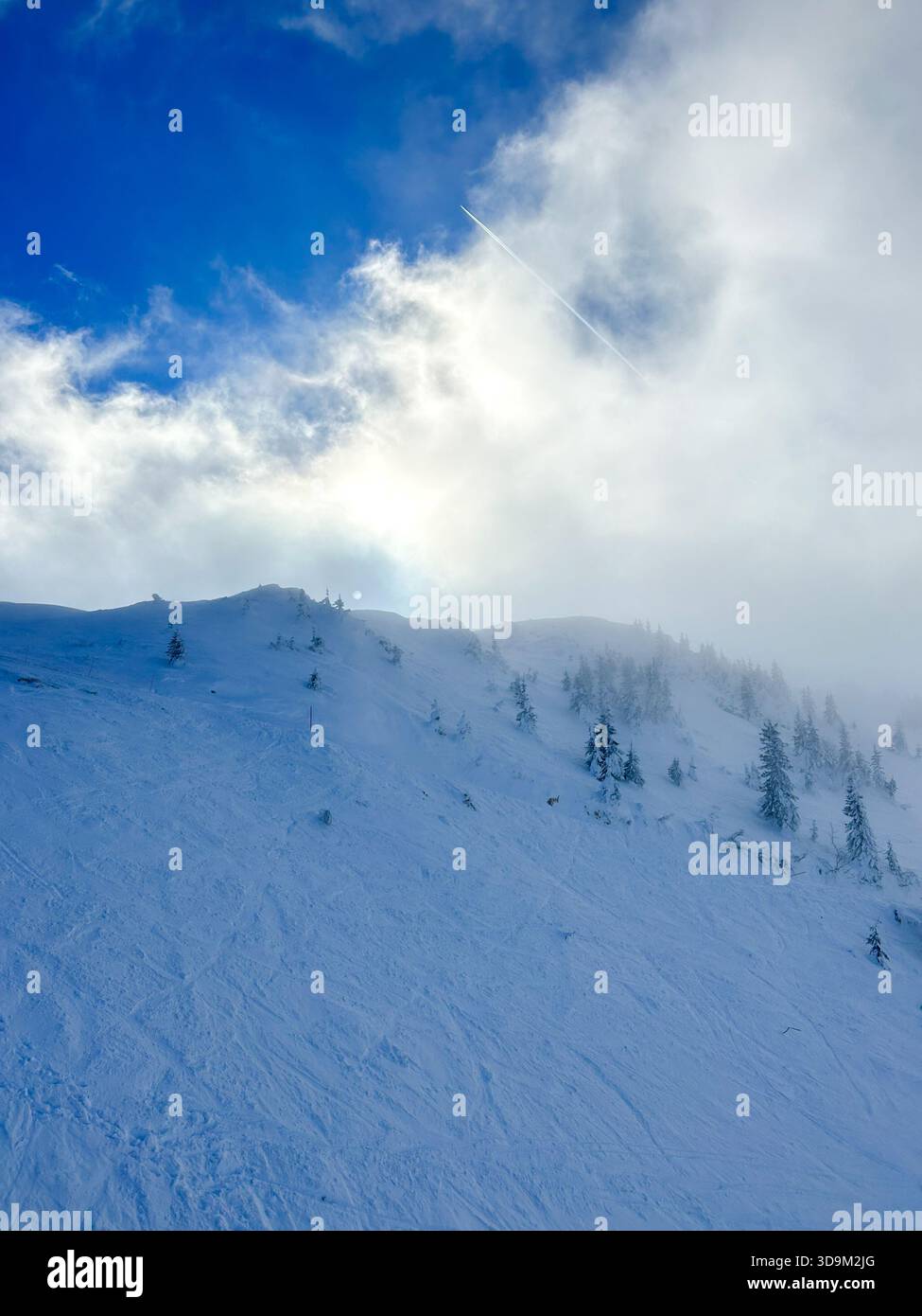 Dramatic winter scene on Jahorina Mountain with clouds moving over a snowy slope, evergreen trees, and a bright blue sky breaking through. - Smartphone Captured Stock Image