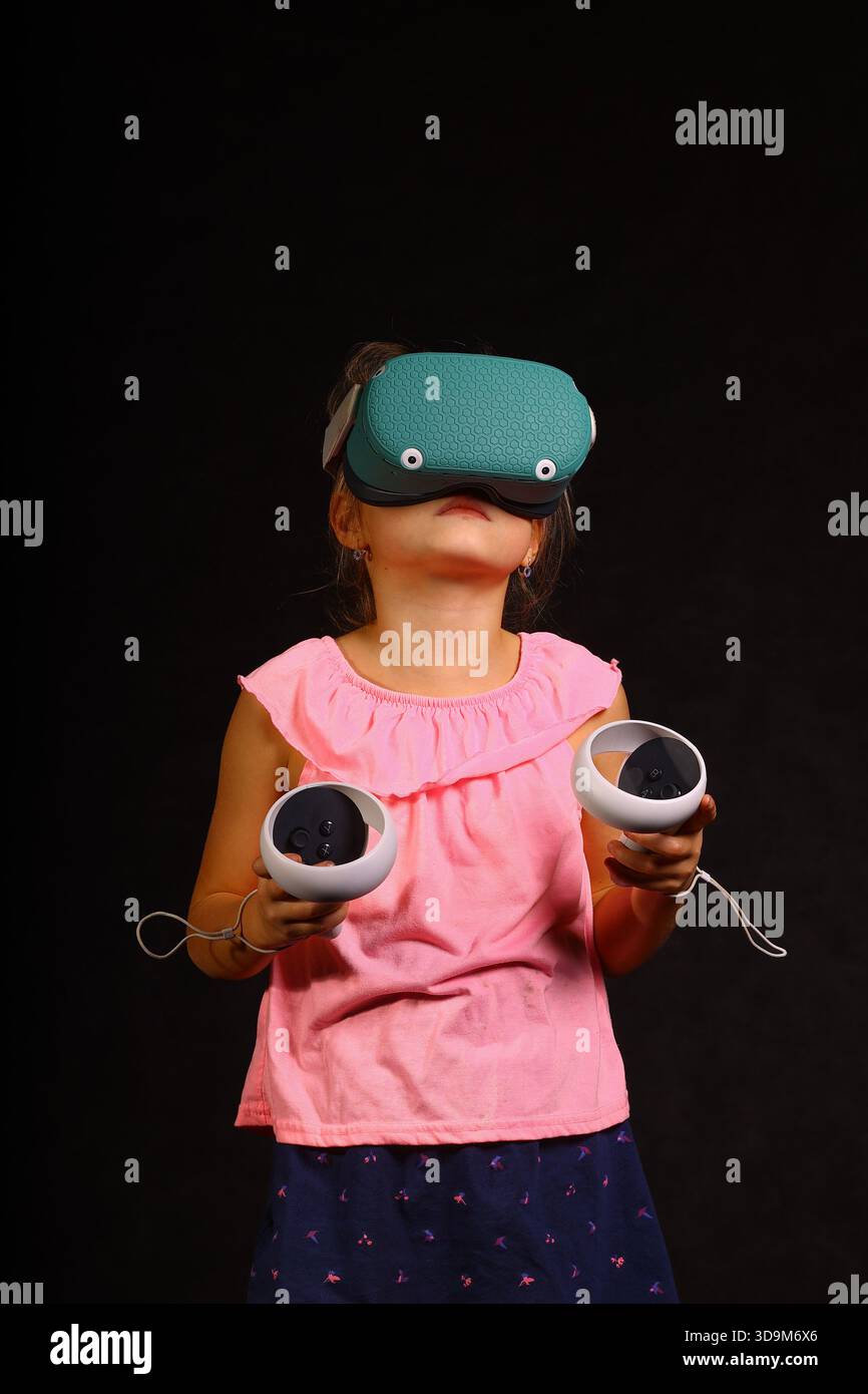 Child using virtual reality headset with motion controllers during immersive VR gaming experience on dark studio background Stock Photo