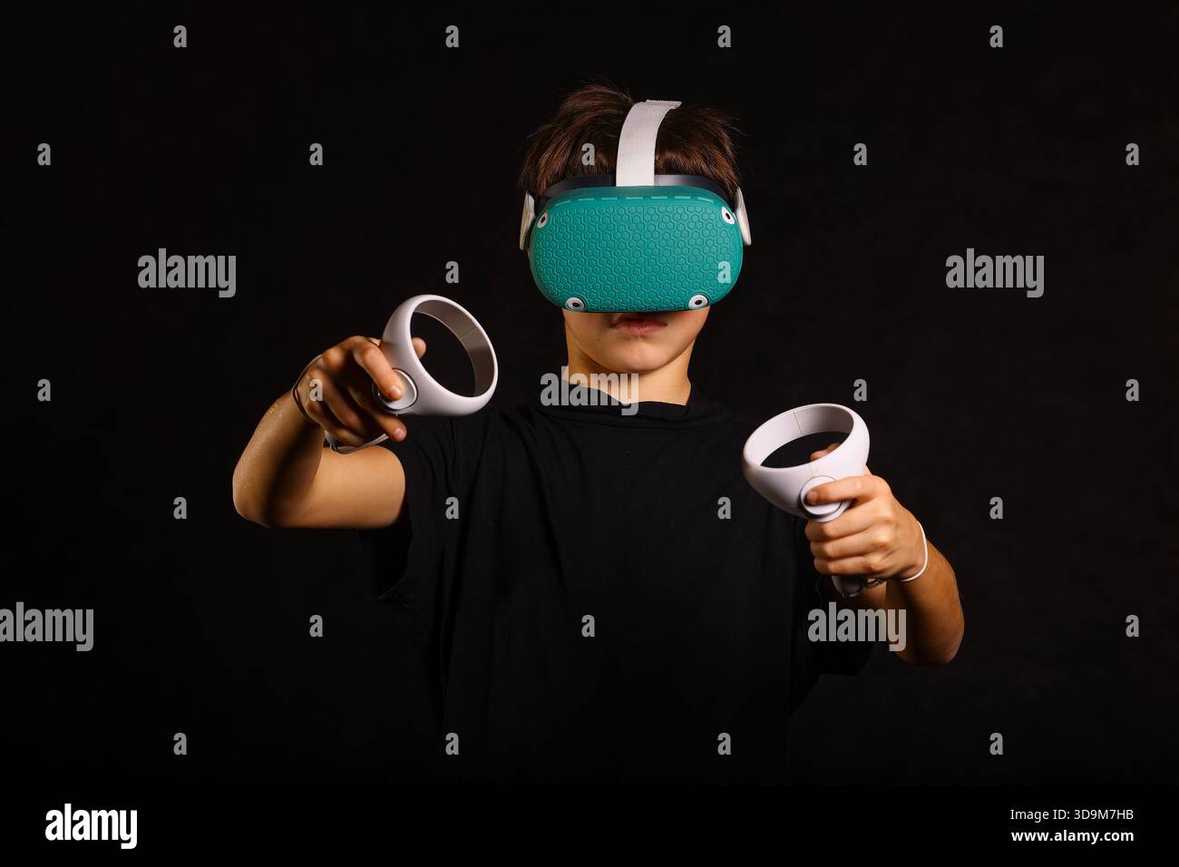 Boy engaged in virtual reality game, holding both controllers forward while concentrating on gameplay. Stock Photo