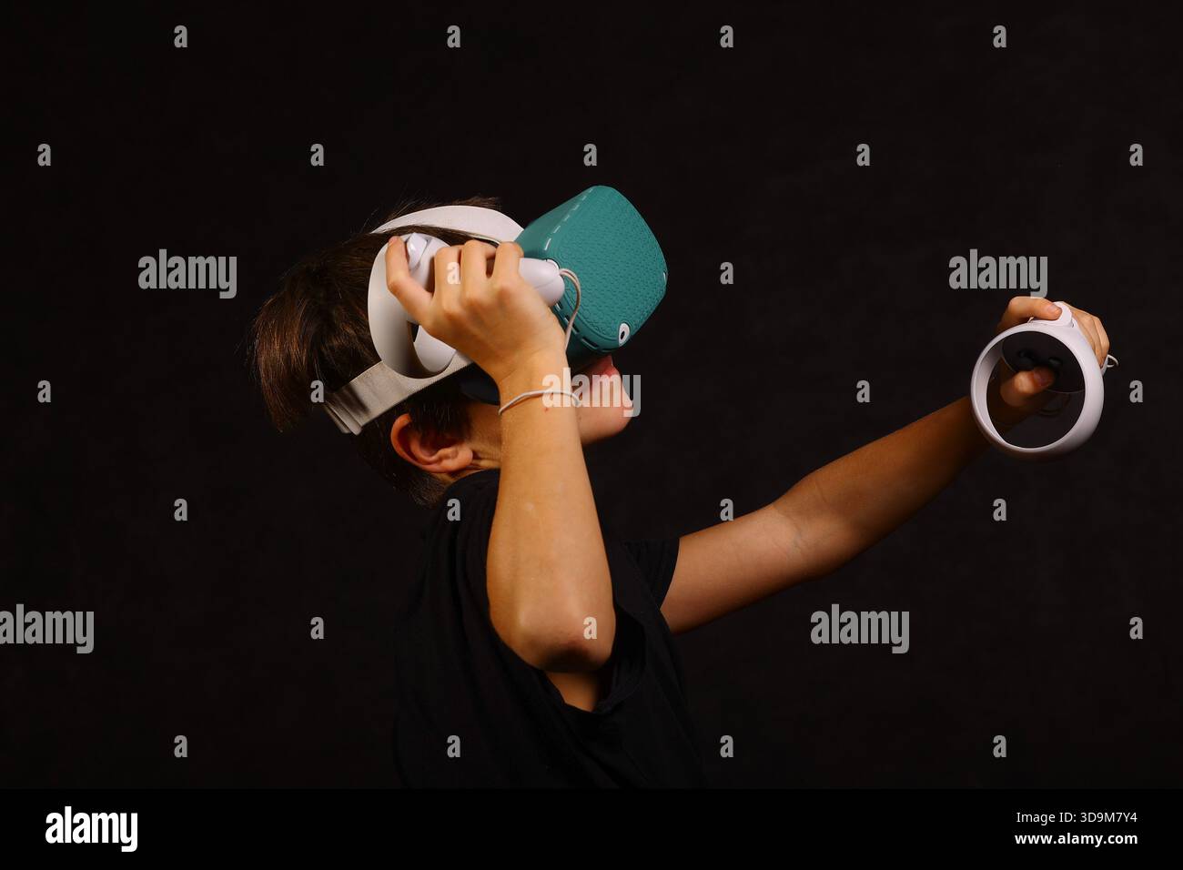Boy lifting VR headset while holding controller, exploring virtual world and interactive gaming technology. Stock Photo