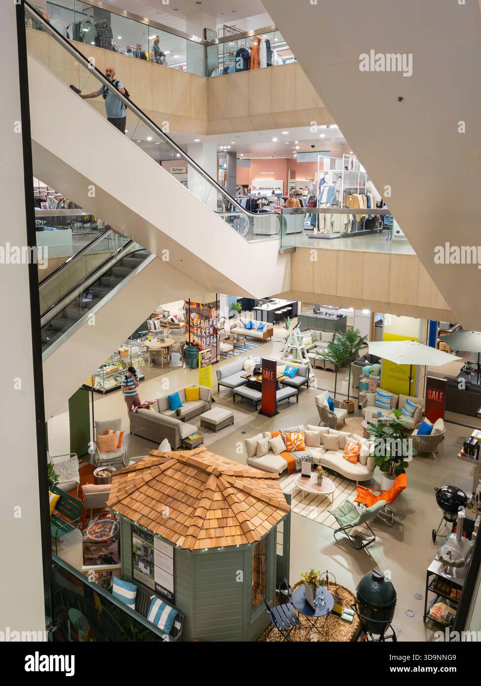 Escalators between floors in John Lewis department store, Broad Street, Reading, looking down on an open plan floor with seasonal garden furniture, UK - Smartphone Captured Stock Image