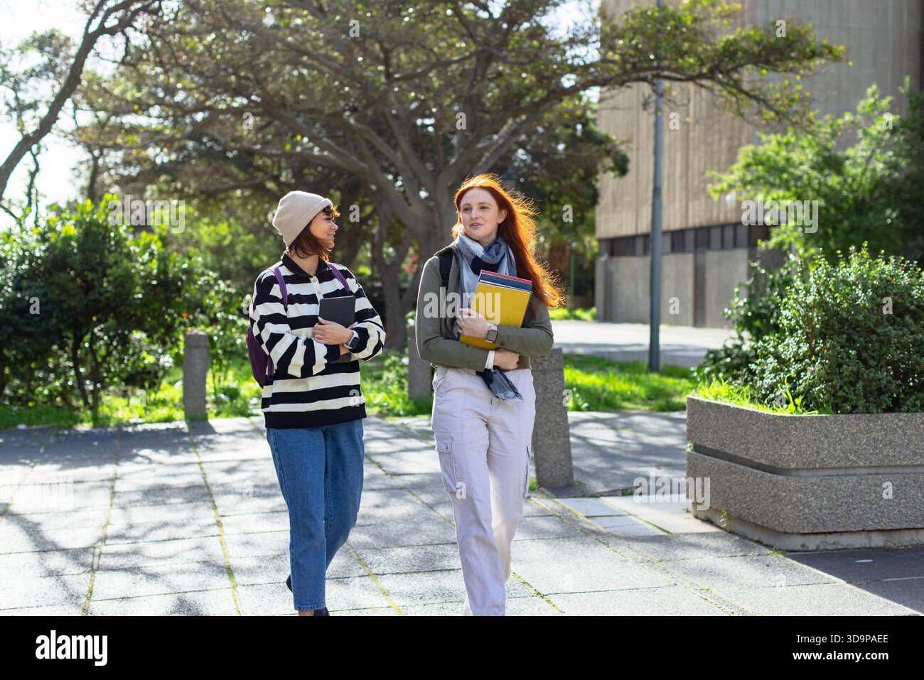 Diverse female students walking on campus pathway carrying tablet and ...