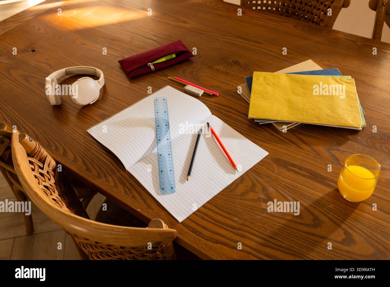 Open lined notebook sitting centered on wooden dining table with blue ruler and pencils Stock Photo