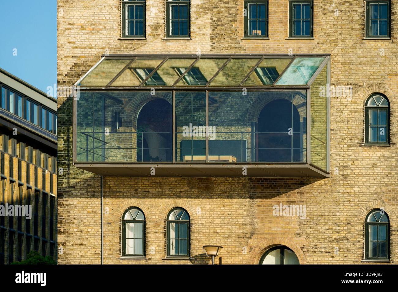 A light brown brick building features a refined glass balcony extension ...