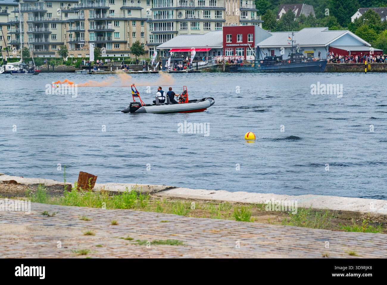 A sea demonstration with a rubber rescue boat, orange smoke rising from a floating flare, yellow buoys in the water, distant ships in the background i Stock Photo