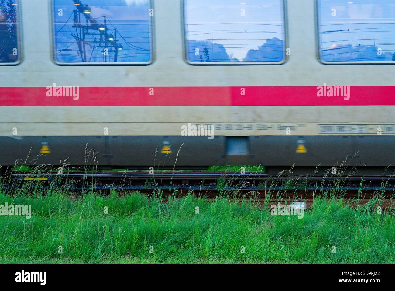 A White Deutsche Bahn Train With A Large Red Stripe Rushes Along The a-white-deutsche-bahn-train-with-a-large-red-stripe-rushes-along-the