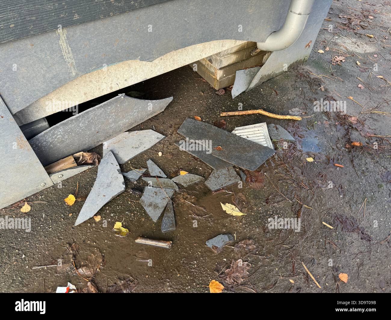 Broken pieces of slate scattered on the ground near a building's foundation. Stock Photo