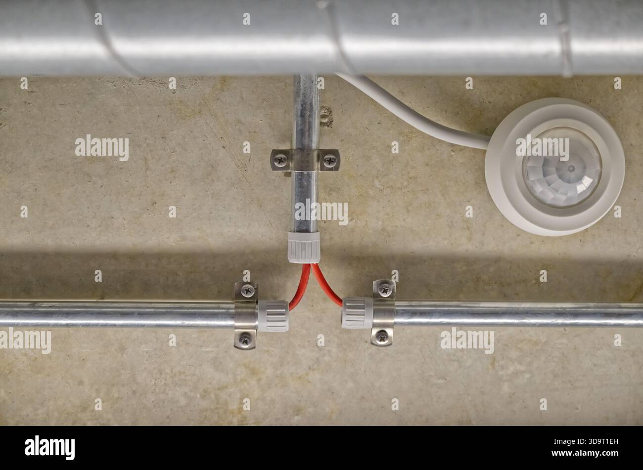 Ceiling-mounted motion sensor with exposed electrical wiring in a conduit. Stock Photo