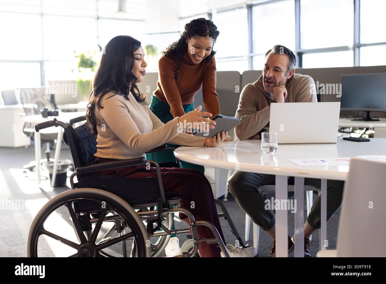 Diverse coworkers collaborating around round table in modern office using tablet and laptop Stock Photo
