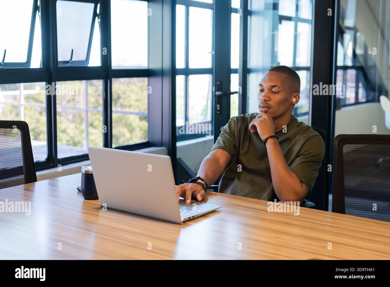African American man sitting at wooden table in modern office typing on silver laptop, copy space Stock Photo