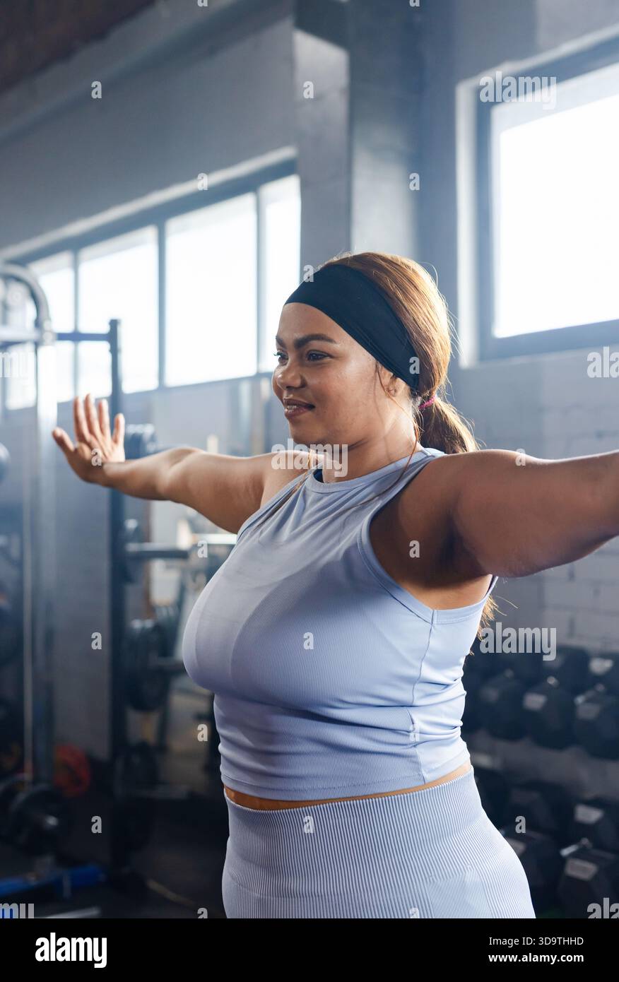 Female Rack Attack Mid adult female holding arms out in gym, wearing light blue workout ...