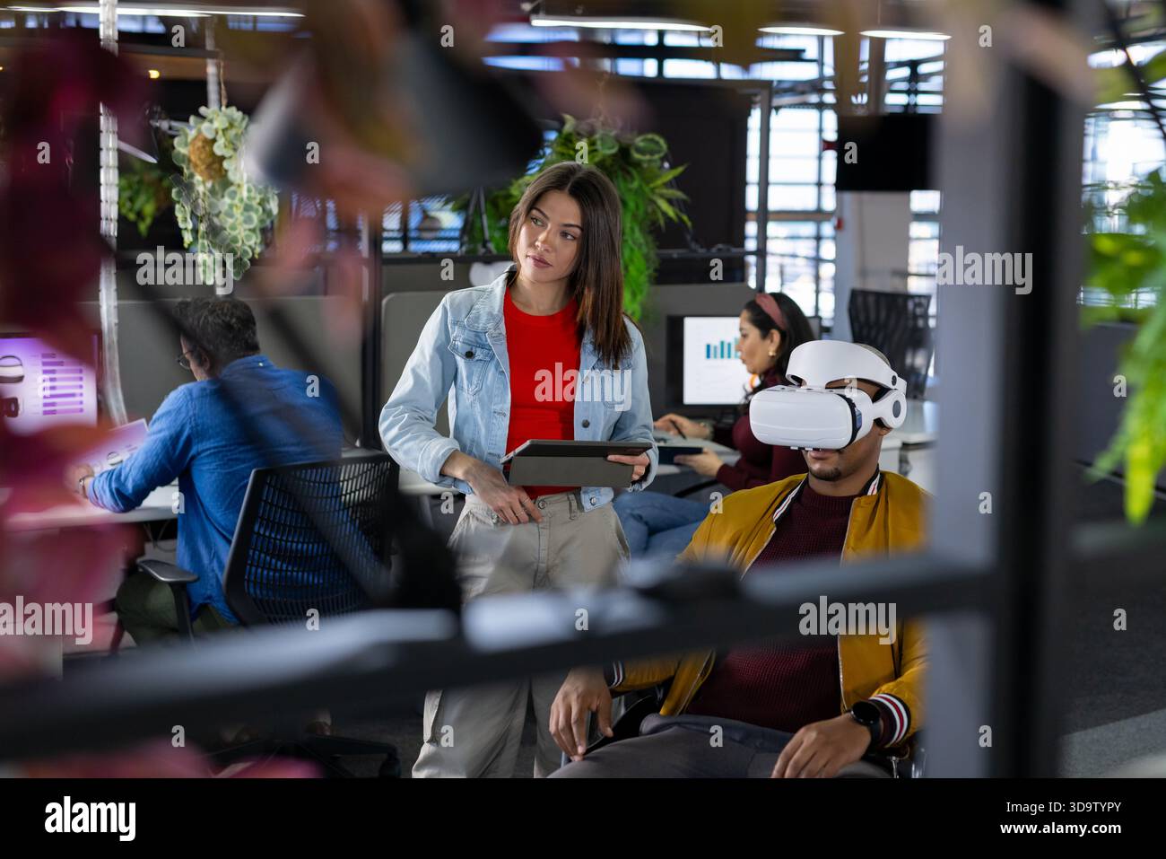 Diverse coworkers presenting virtual reality project in open-plan office using tablet and computers Stock Photo