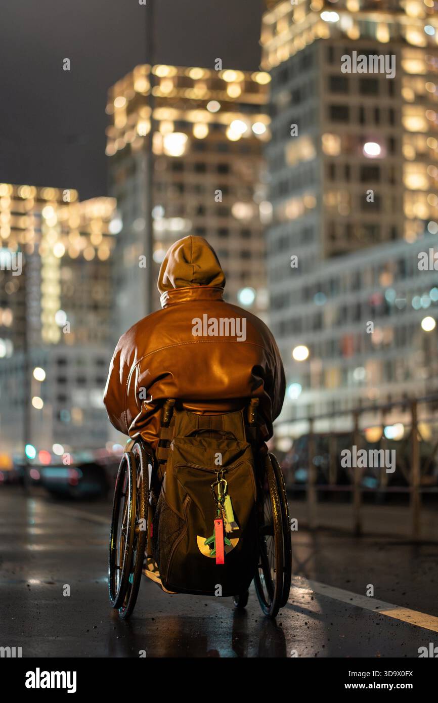 Unrecognizable disabled man in wheelchair with hood on and backpack ...