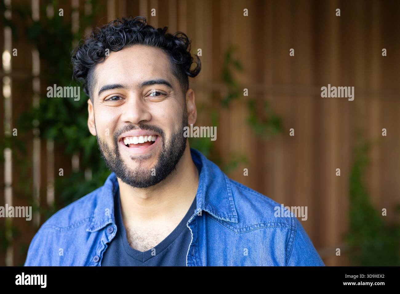 Man standing and smiling at camera in backyard garden wearing denim shirt over v-neck Stock Photo