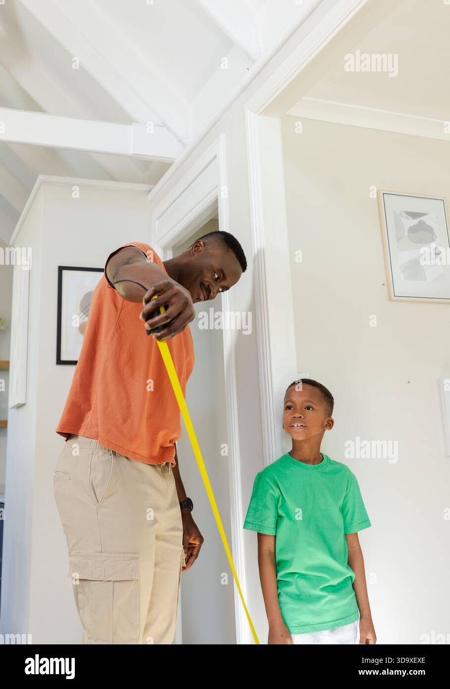 African American father and son measuring height by doorframe in hallway with yellow tape measure Stock Photo
