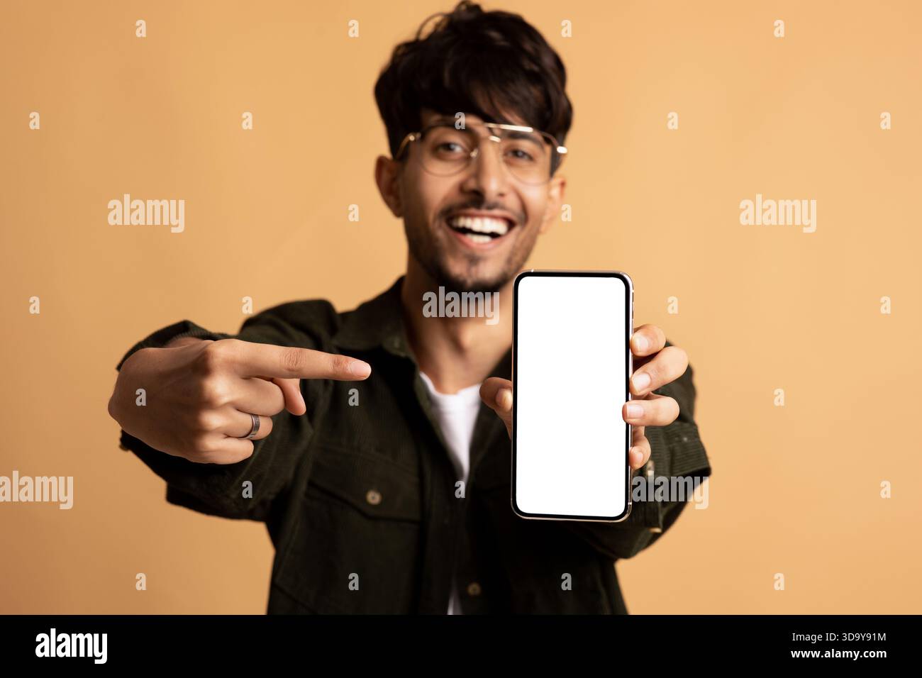 Young Man Smiles and Points at His Smartphone Against a Warm Background Stock Photo