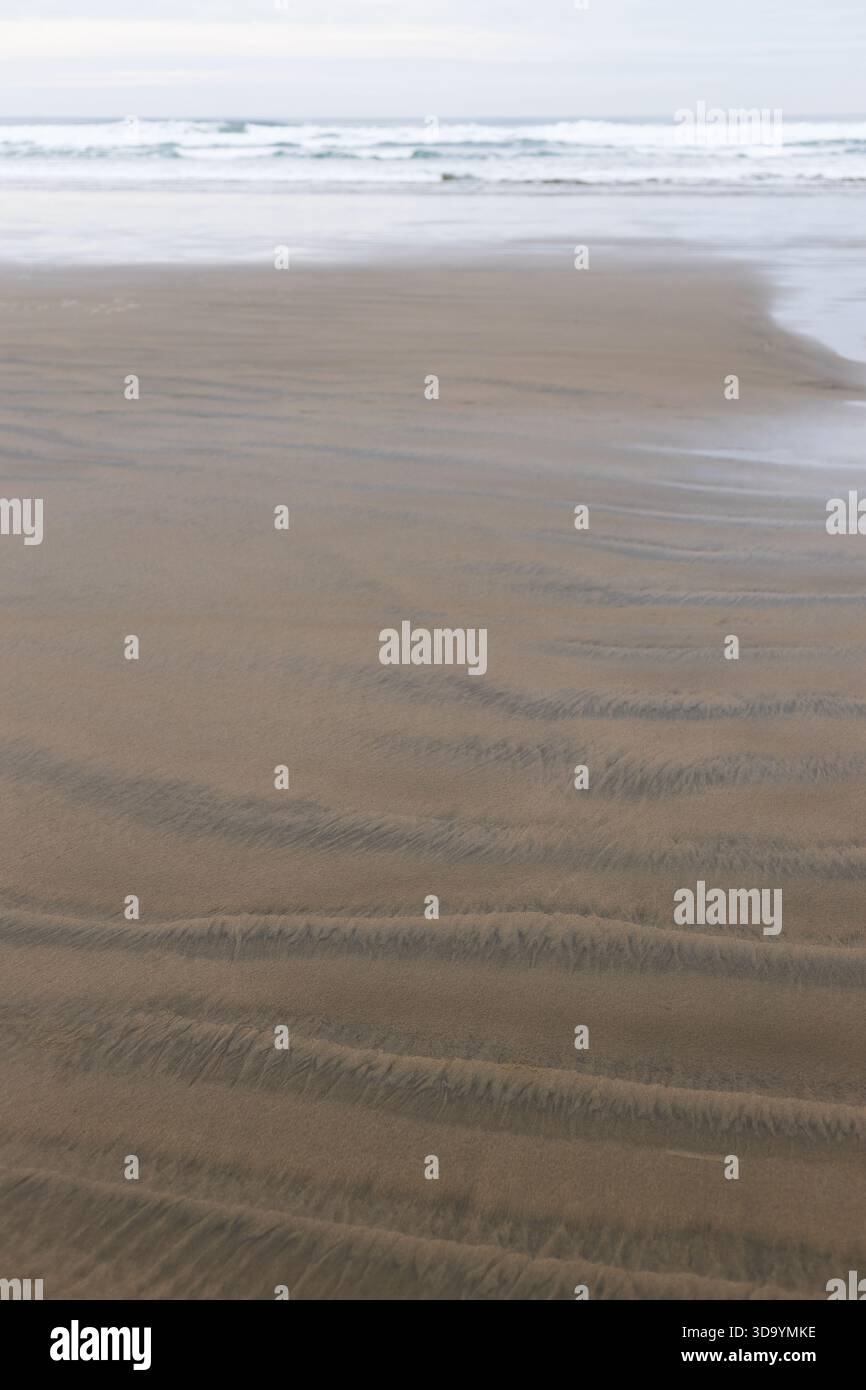 Rippled pattern in sand on a beach, with waves in background. Stock Photo