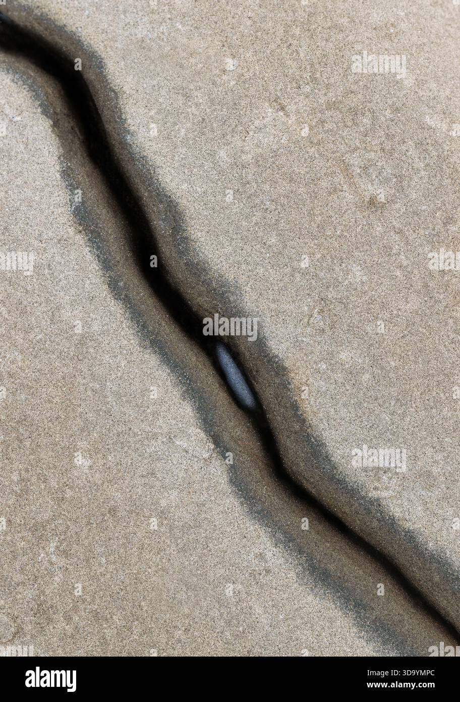 A black stone in the crack of a large rock. Stock Photo